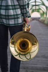 Musician walking on a bridge with his horn in his hand.