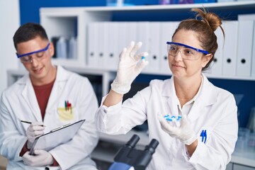 Man and woman scientists write on document holding pills at laboratory