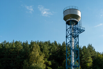 New modern water tower on the background of blue sky and forest. Methods of water storage for irrigation of agricultural crops in difficult climatic and weather conditions. A barrel with water