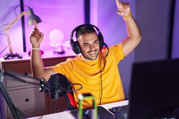 Young hispanic man streamer playing video game dancing at gaming room