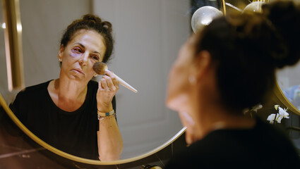 Middle age hispanic woman using makeup to cover signs of domestic violence at bathroom