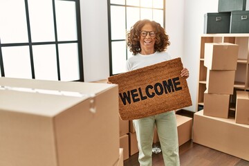 Middle age hispanic woman smiling confident holding welcome doormat at new home