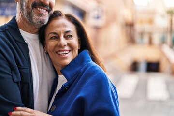 Middle age man and woman couple hugging each other standing at street