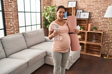 Fototapeta na wymiar Young pregnant woman holding yoga mat at home celebrating crazy and amazed for success with open eyes screaming excited.