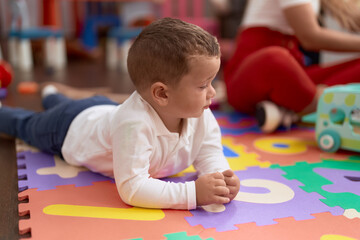 Adorable toddler lying on floor with relaxed expression at kindergarten