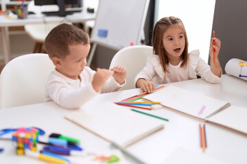 Adorable girl and boy drawing on notebook sitting on table at kindergarten