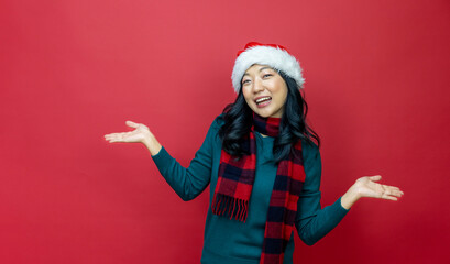 Fototapeta na wymiar Pretty smiling asian woman in warm christmas sweater and santa hat is having excitement on red background for season celebration concept with copy space 