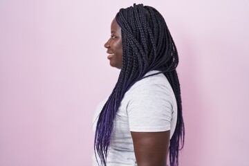 Young african woman standing over pink background looking to side, relax profile pose with natural...