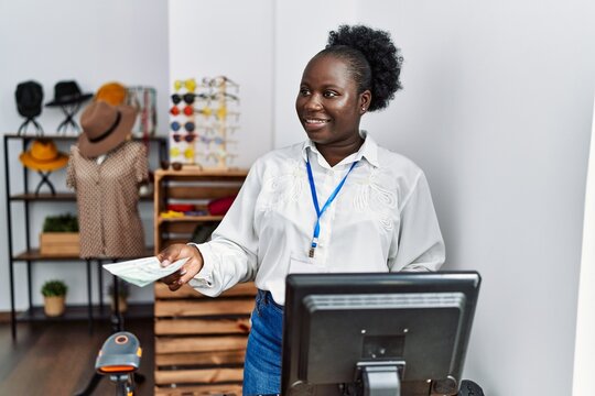 Young african american woman shopkeeper smiling confident holding dollars at clothing store