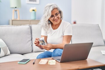 Middle age woman counting banknotes sitting on sofa at home