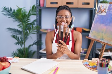 African american woman smiling confident holding paintbrushes at art studio
