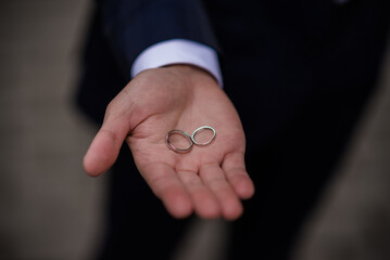 Groom holding wedding rings in hand. Two wedding rings on the floor with contrast wedding rings on floor, on ground, on piano, in hand