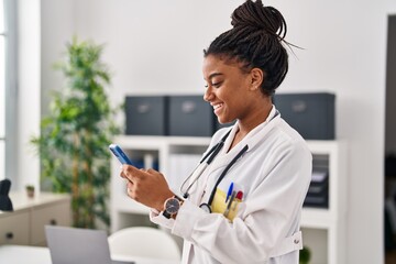 African american woman wearing doctor uniform using smartphone working at clinic