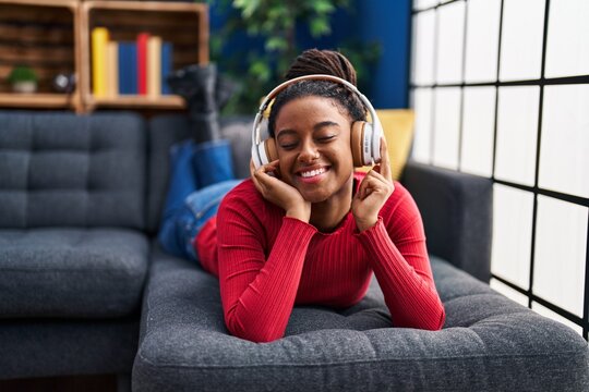 African American Woman Listening To Music Lying On Sofa At Home