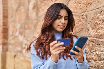 Young hispanic woman using smartphone and credit card at street