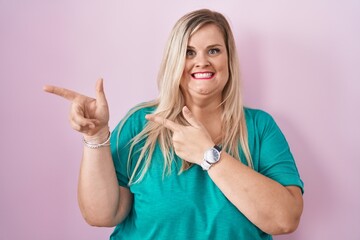 Caucasian plus size woman standing over pink background pointing aside worried and nervous with both hands, concerned and surprised expression