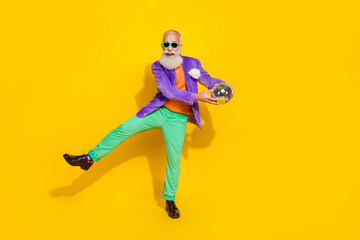 Full length photo of funny cheerful man wear purple velvet jacket dancing holding discotheque ball walking isolated yellow color background