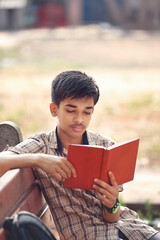Indian teenage boy reading book in park	
