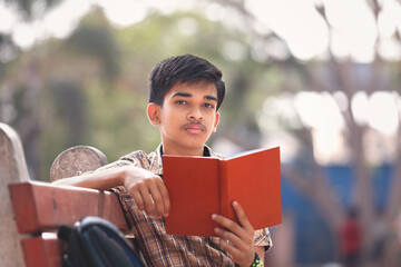 Indian teenage boy reading book in park	
