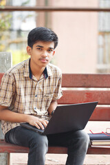 Portrait of Indian boy using laptop while attending the online classes in park
