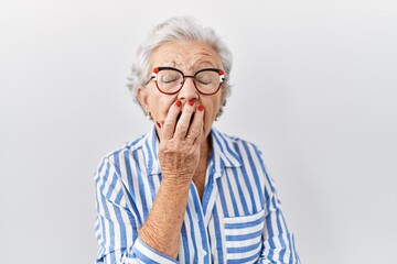 Senior woman with grey hair standing over white background bored yawning tired covering mouth with hand. restless and sleepiness.