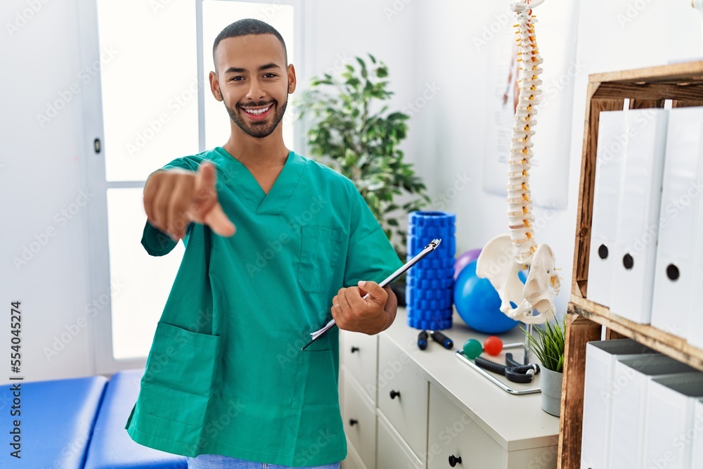 Poster african american physiotherapist man working at pain recovery clinic pointing to you and the camera 