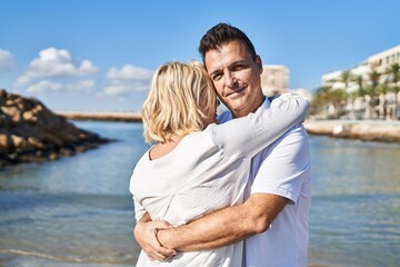 Middle age man and woman couple hugging each other standing at seaside