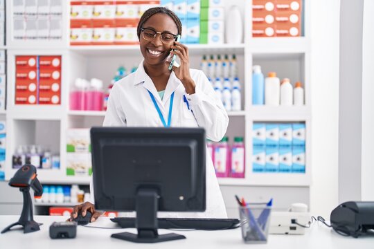 African american woman pharmacist talking on smartphone using computer at pharmacy
