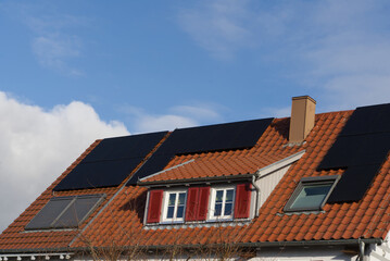 A residential building roof with dormer and skylights. Modern solar modules are laid on the tiled...