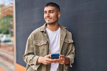 Young hispanic man smiling confident using smartphone at street