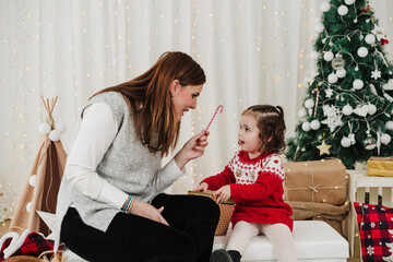 cheerful mother and daughter at home enjoying christmas time at home. giving candy to child