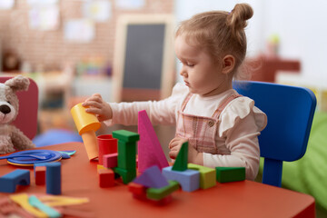 Adorable caucasian girl playing with construction blocks standing at kindergarten