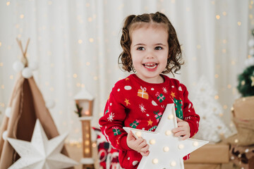 smiling little girl at home holding star during christmas time