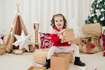 cheerful little girl at home during christmas time holding gift box