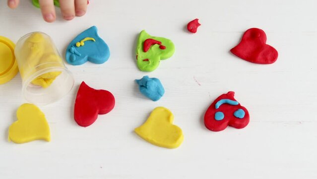 many clay plasticine colorful hearts on table and kids hand putting smile face eyes.emoticon smiling heart shape valentine's day diy do it yourself home kindergarten or school activities.love concept