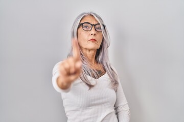 Middle age woman with grey hair standing over white background pointing with finger up and angry expression, showing no gesture