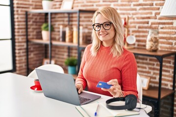 Young blonde woman smiling confident using laptop and credit card at home