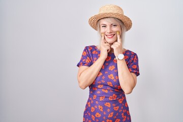 Young caucasian woman wearing flowers dress and summer hat smiling with open mouth, fingers pointing and forcing cheerful smile