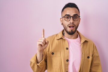 Young hispanic man standing over pink background pointing finger up with successful idea. exited and happy. number one.