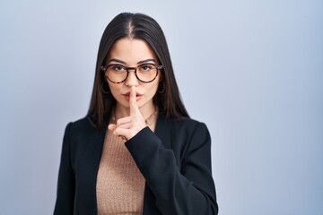Young brunette woman standing over blue background asking to be quiet with finger on lips. silence...