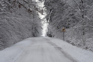 Znak ostrzegawczy, ostry zakręt, zima i ośnieżona droga. Trudne warunki do jazdy.