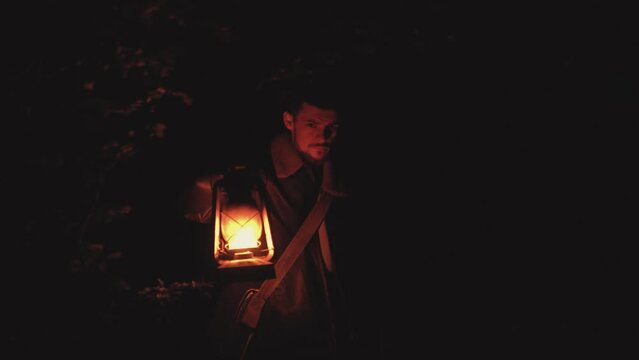 Adult afraid man with beard wear retro clothes travel a night. Seriously guy walking on the dark forest use vintage kerosene lamp try to find exit.