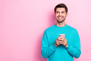 Photo of young funny attractive handsome businessman wear cyan pullover hold phone look interested eshop offer isolated on pink color background