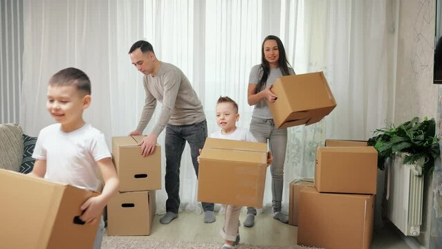 Family carries carton boxes with belongings moving into new apartment together. Parents and boy children enjoy moving together into purchased flat
