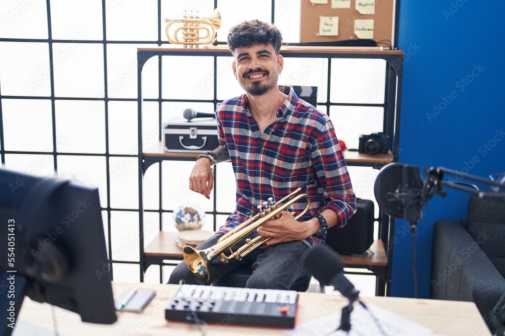 Sticker Young hispanic man musician holding trumpet at music studio