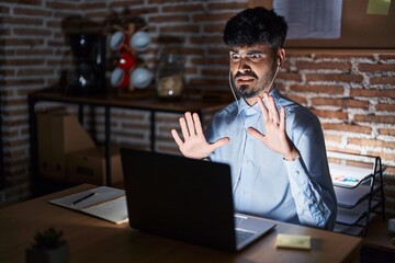 Young hispanic man with beard working at the office at night afraid and terrified with fear expression stop gesture with hands, shouting in shock. panic concept.
