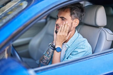 Young hispanic man stressed driving car at street