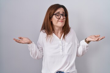 Brunette woman standing over white isolated background clueless and confused expression with arms and hands raised. doubt concept.