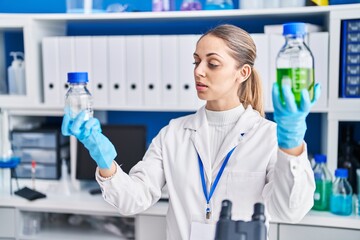 Young woman scientist holding bottles with liquid at laboratory