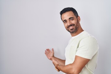 Hispanic man with beard standing over isolated background inviting to enter smiling natural with open hand